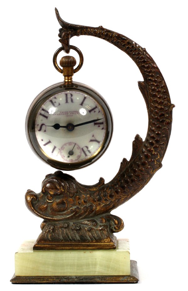 PATINATED METAL & ONYX BULL'S EYE DESK CLOCK: NEOCLASSICAL STYLE PATINATED METAL & ONYX BULL'S EYE DESK CLOCK, SHERIFF'S JURY PANEL, 1900, H 7 3/4:Gilt metal dolphin raised on an onyx base, having a bull's eye clock suspended from its tail. The t