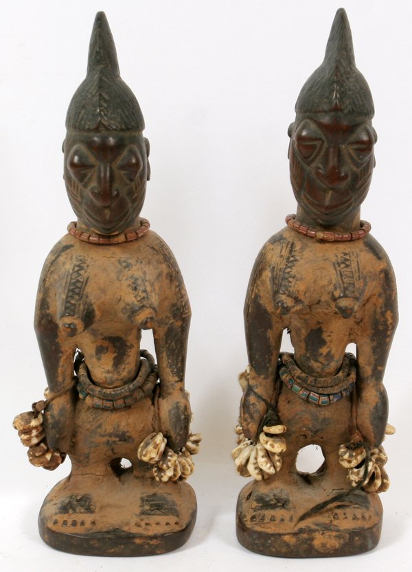 AFRICAN YORUBA IBEJI TWIN STATUES 2 PCS: AFRICAN YORUBA, IBEJI TWIN STATUES, 2 PCS H 11": From the Yoruba tribe, Nigeria. The figures have curved shoulders above protruding, pointed breasts. They are carrying bundles of cowry shells in both 