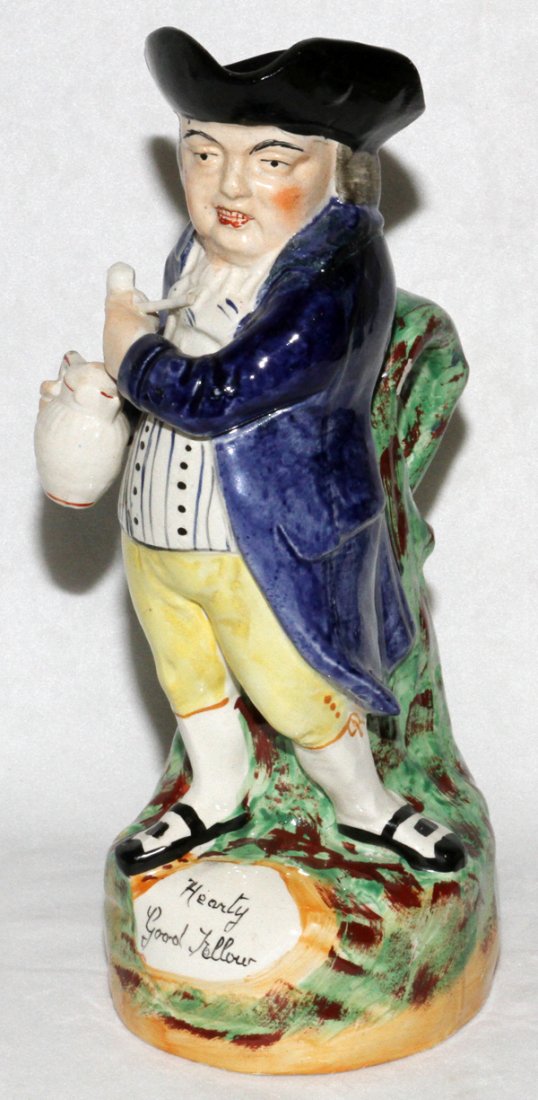STAFFORDSHIRE 'HEARTY GOOD FELLOW' TOBY JUG: STAFFORDSHIRE 'HEARTY GOOD FELLOW' TOBY JUG, MID 19TH C., H 12":In the form of a standing man holding a pipe in left hand and a jug of ale in his right hand, with "Hearty Good Fellow" painted on the b