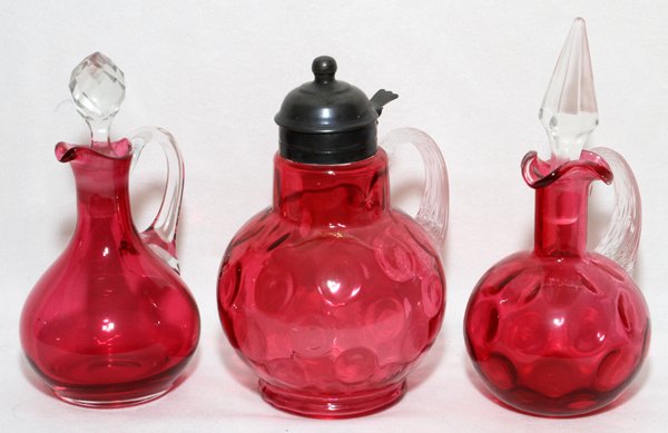 VICTORIAN CRANBERRY GLASS CRUETS & SYRUP JUG: VICTORIAN CRANBERRY GLASS CRUETS & SYRUP JUG, LATE 19TH C., THREE PIECES, H 7":Including 2 cruets with clear handles and stoppers, and 1 syrup jug with metal mounts.
