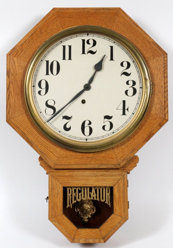 REGULATOR SCHOOL WALL CLOCK: REGULATOR SCHOOL WALL CLOCK, H 25" W 17", D 2":having a white oak case with an octagonal shape and glass hinged access door opening to a white face with Arabic numerals one key wind. Lower hinged acce