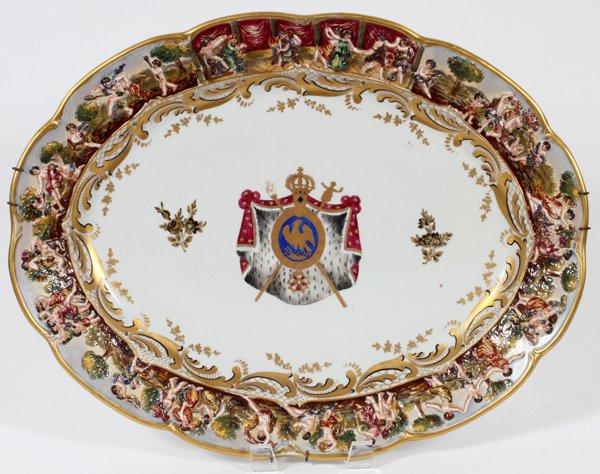 CAPODIMONTE PORCELAIN PLATTER/CHARGER: CAPODIMONTE PORCELAIN PLATTER/CHARGER, H 2.25", L 17", D 13":Having a central flag with coat of arms and a figural border in relief. Marked on the reverse "Are Roi de Rome, Naples, 1811". For a high r