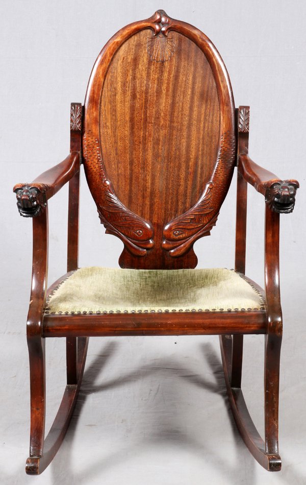 MAHOGANY ROCKING CHAIR EARLY 20TH C.: MAHOGANY ROCKING CHAIR, EARLY 20TH C., H 34", W 28":An oval back with carved dolphin motif above an upholstered seat flanked by open arms with carved mask terminals. For a high resolution photo