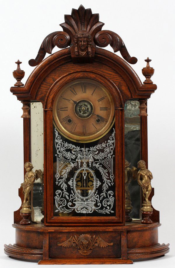 ANSONIA CLOCK CO. CARVED WOOD & BRASS MANTEL CLOCK: ANSONIA CLOCK CO. CARVED WOOD & BRASS MANTEL CLOCK, H 24 1/4", W 16 1/2":Having roman numerals about the clock face, a painted stencil design at the pendulum window, two key wind, and flanked by two n