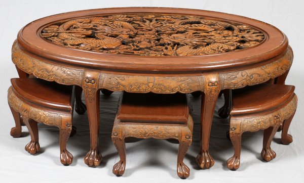 CARVED TEAKWOOD COFFEE TABLE & STOOLS 7 PIECES: CARVED TEAKWOOD COFFEE TABLE & STOOLS, 7 PIECES, H 21", W 48", D 29":Having an oval glass top covering deep carved dragons and flowers, with six matching triangular shape stools that fit under the tab