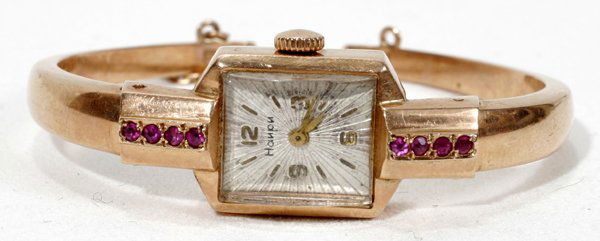 ART DECO GOLD & RUBY LADY'S BRACELET WATCH: ART DECO 14KT YELLOW GOLD & RUBY LADY'S BRACELET WATCH, C. 1940:14kt yellow gold case and hinged wrist band with safety chain, flanked by eight round cut rubies, convex crystal, dial appears to be mar