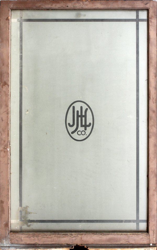 J L HUDSON WINDOW: J L HUDSON WINDOW, H 85" W 54":Frosted glass with stylized 'JLH' logo inside an oval in black. Black border around the edge. Size includes frame.