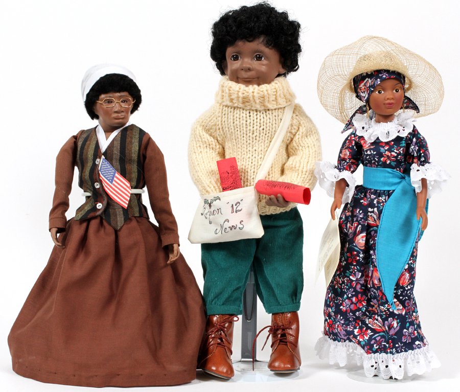 'REGION 12' BLACK DOLLS 1989 THREE: 'REGION 12', BLACK DOLLS, 1989, THREE, H 15.6", 14", 14':Modern news boy doll with knit sweater, lady in brown outfit by Sharon Napin, Caribbean lady. Encised on doll with brown dress: "Sojourner Trut