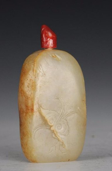 Jade Snuff Bottle w/ Brown Skin, 18th Century: Jade snuff bottle with brown mottling from the 18th century. The snuff bottle is carved in a natural, rectangular form. It is incised with lingzhi, flowers, and boulders. It has a red stopper and a sp
