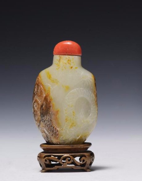 White Jade with Brown Skin Snuff Bottle, 19th Century: This white jade with brown skin snuff bottle from the 19th century is ornately carved with a snake, sun, and flowers. It has a stopper with a spoon. Dimensions are 2 inches wide by 2 3/4 inches high. 