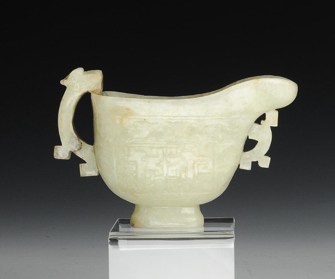 Jade Cup with Handle, Ming Dynasty: Jade cup with handle from the Ming dynasty. The pale green jade has brown striations through it. The cup is carved with geometric patterns and chilong on either side. Near the spout, it is carved with