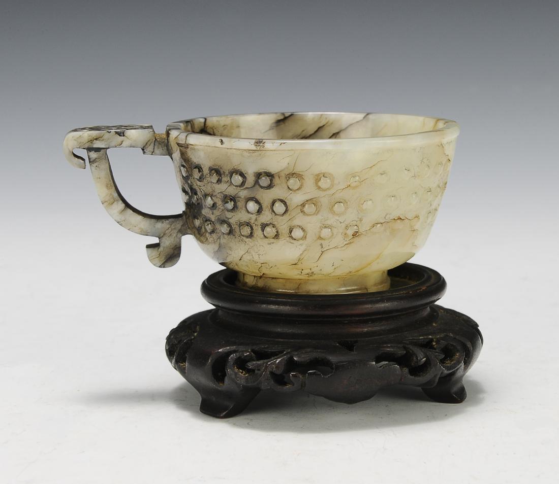 Jade Cup w/ Handle, Ming Dynasty: Grey jade cup with a handle from the Ming dynasty. The cup is carved with raised circles on the exterior and the handle is curved with a ruyi head design carved into the top. It has a straight foot an