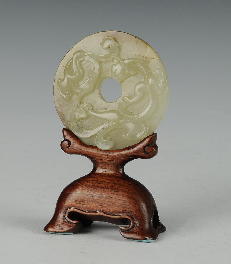 Carved Jade Bi with Wood Base, 18th - 19th Century: Carved jade bi from the 18th - 19th century. This bi is carved on one side with two sinuous chilong. The obverse side is carved with a millet pattern. It comes with a fitted, decorative wooden stand. 