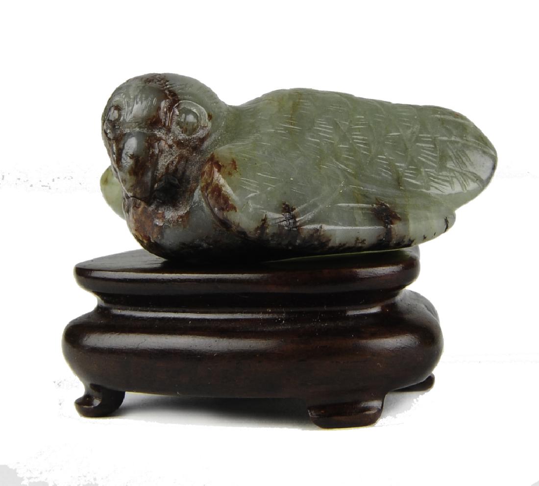 Jade Carving of a Bird, Ming Dynasty or Earlier: Jade carving of a bird from the Ming dynasty or earlier. Carved out of celadon jade with brown mottling in the form of a resting bird with a curved beak. It comes with a wooden stand. Dimensions are 1