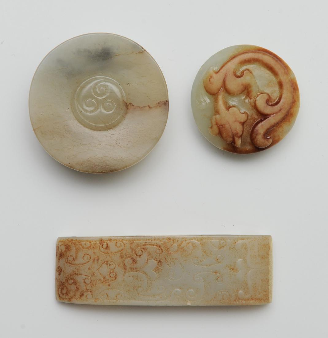 Trio of Jade Carvings, Ming Dynasty or Earlier: Trio of jade carvings from the Ming dynasty or earlier. Includes: a jade sword pommel, a jade chilong button, and a jade buckle. The grey jade pommel is carved with a central swirling design and is ro