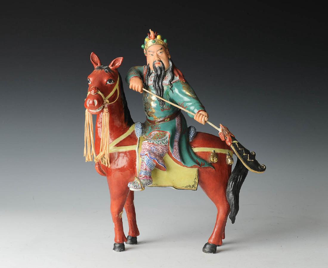 Guan Gong & Horse Figure: A porcelain figurine of Guan Gong on horseback holding a spear. Fabric tassels hang from the horse's bridle, and Guan Gong wears a headdress and elaborate costume embellished with gold-toned paint. Di