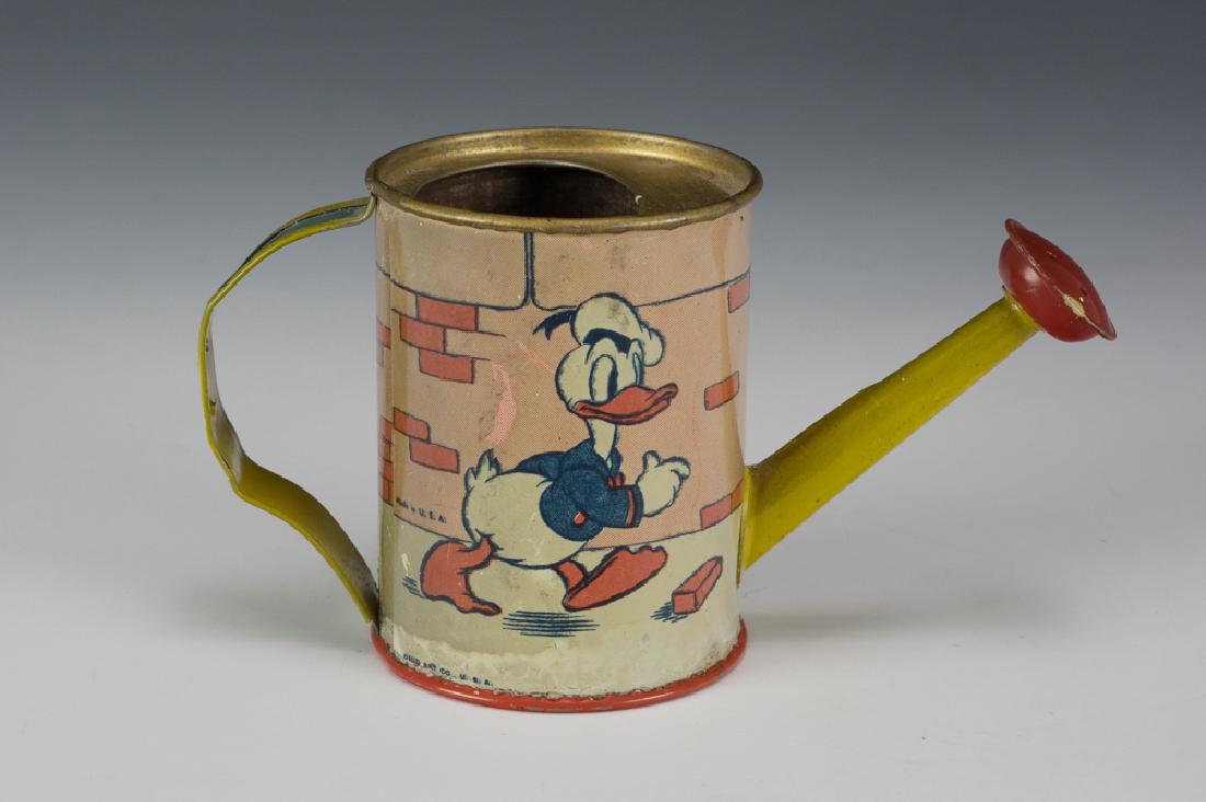 Donald Duck Watering Can by Ohio Art 1938: A toy watering can featuring Donald Duck tripping over a brick. The bottom is marked "1939, W. D. Ent." and "Ohio Art Co. USA" Dimensions are: 3" tall X 2 3/8" diameter. All measurements are approxima