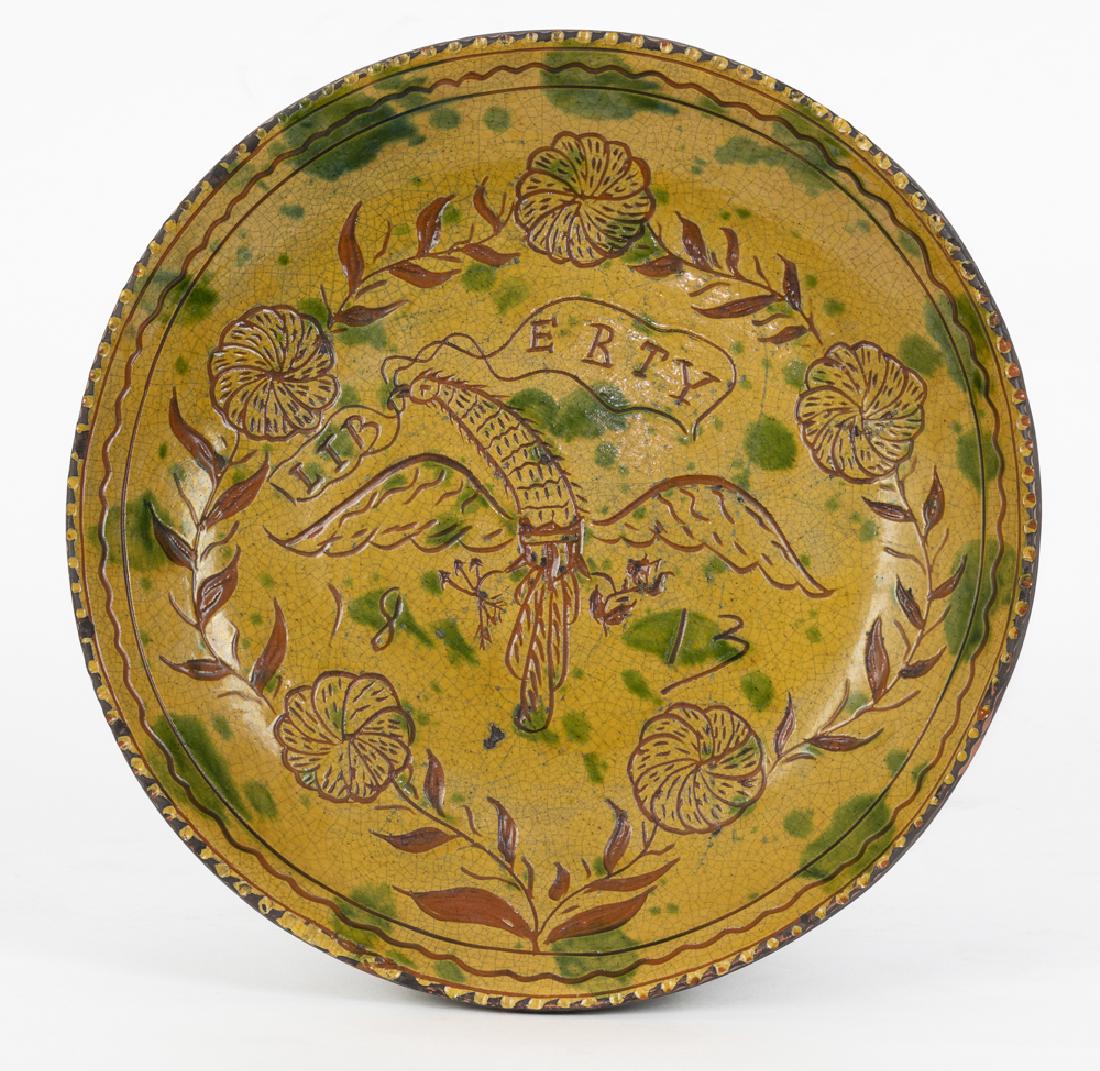 Greg Shooner Sgrafitto Redware Plate, 2000: Decorated with flowers and the American Eagle clutching a Liberty banner. The bottom is signed by Greg Schooner and dated 2000. It is also stamped with "Schooner, American Redware" and a notice that t