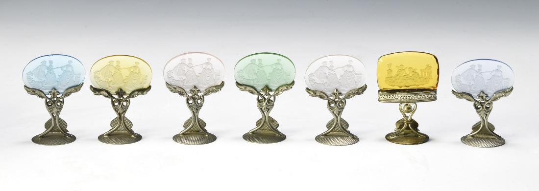 Seven Czech Glass Intaglio Cut Place Card Holders: Bases marked 'Made in Czechoslovakia'. Six have oval inserts with Georgian era scenes and one is rectangular with Putti. Dimensions are: 2" tall. All measurements are approximate. Condition: No noted