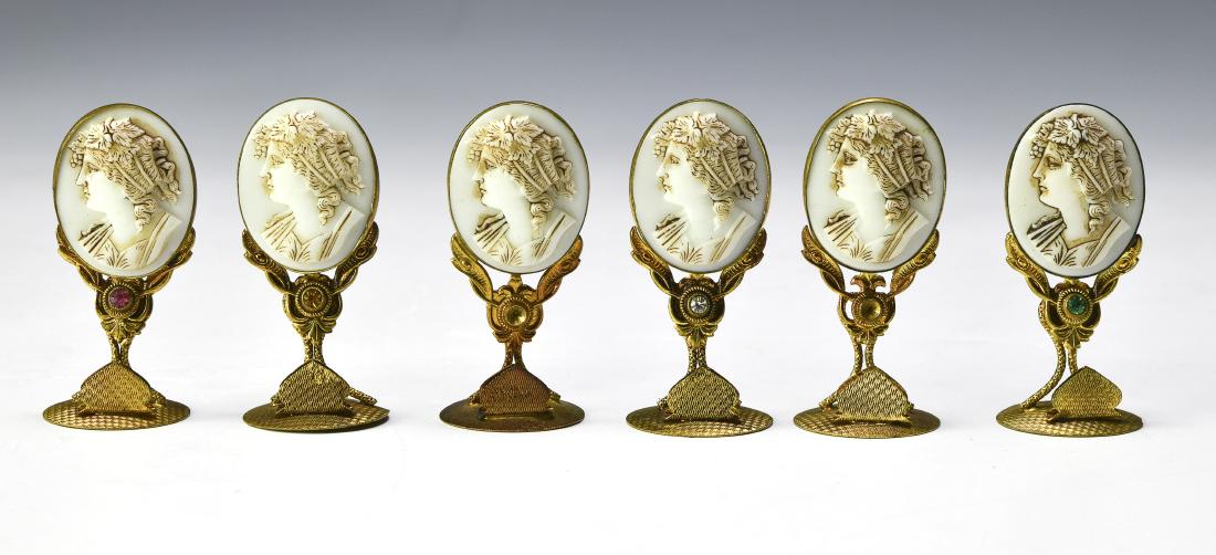 Six Czech Glass Cameo Place Card Holders: Bases marked, 'Made in Czechoslovakia'. Each has a white glass cameo in gilt base and each with different colored "jewel". Dimensions are: 2 1/8" tall. All measurements are approximate. Condition: No