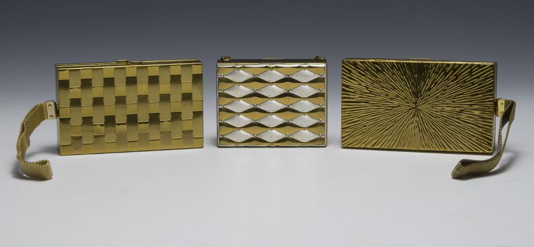 Three Compact Mirror Clutches: Three metal clutches, two in gold metal and one silver/gold metal. One gold clutch is marked 'Evans' and the gold/silver clutch is 'Bell Fifth Avenue'. All three have two compartments that include a m