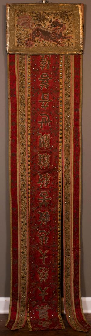 Chinese Couched and Applique Silk Banner: Chinese couched and appliqued silk banner depicting foo-dog with ball against floral background; appliqued pieces are reflective pieces of metal in a circular frame, and two green jewels for the dog's