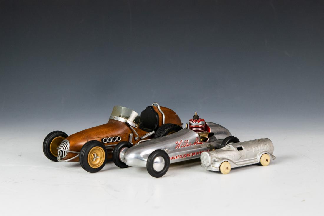 (3) Indianapolis Motor Speedway & Wood Model Car: (3) toy cars, inclduing a Wilbur Shaw Indianapolis Motor Speedway model car with engine and a handmade wooden model of a thimble drome, as well as a base metal miniature Milk Truck, in shape of milk b