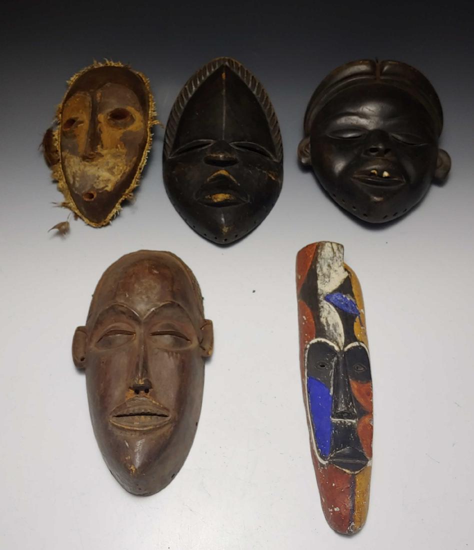 (5) Carved Wood African Masks: Set of 5 African masks; a) in style of Yohure mask from West Africa (Ivory Coast), teardrop shaped face with a border of knotted plant material and feathers, wood surface treated with plaster or mud,