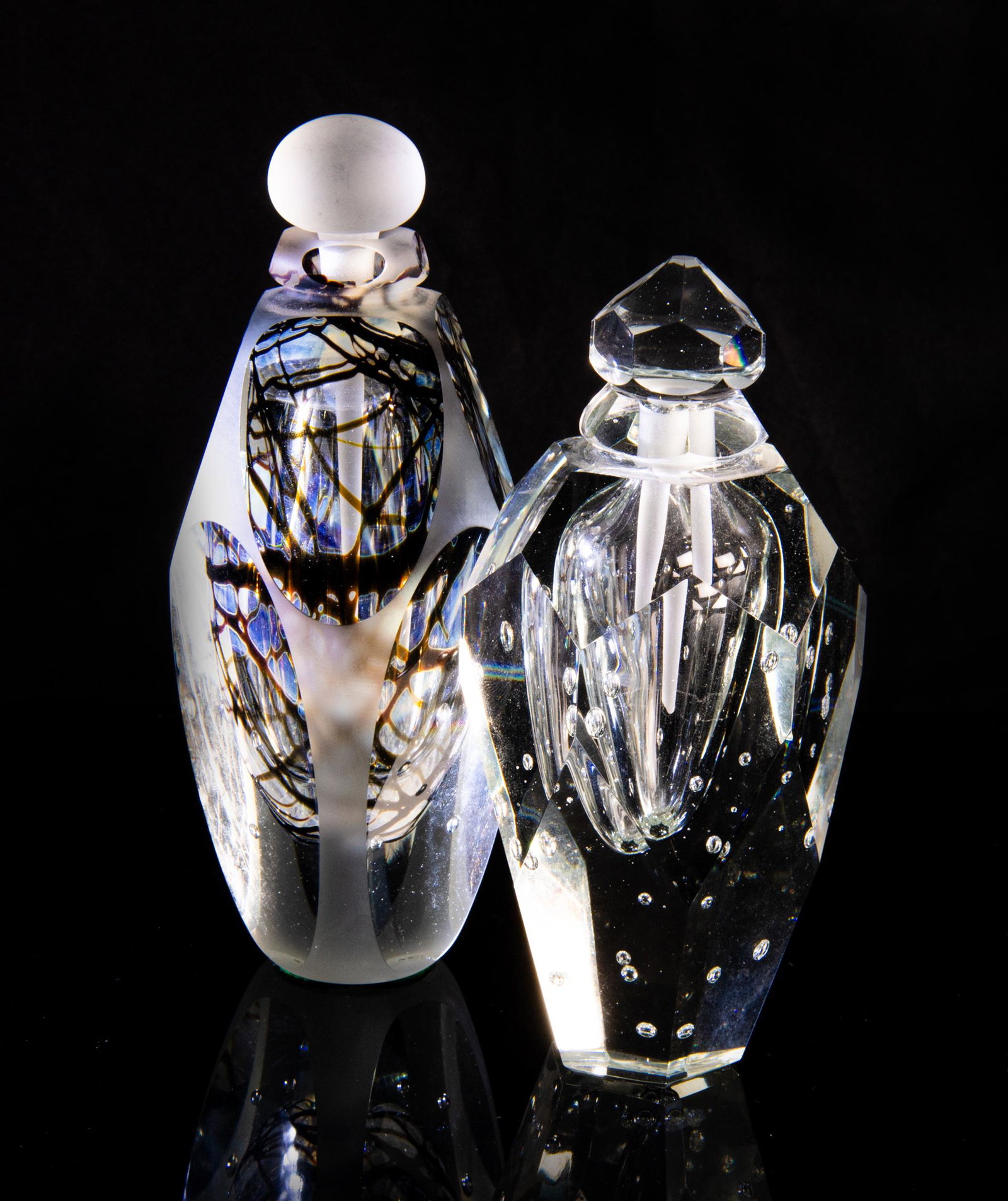 (2) James Clarke Studio Glass Perfume Bottles: Group of (2) James Clarke (American, 20th century) studio glass perfume bottles. One perfume bottle is in all clear glass, while the second is in clear and brown glass. Clear glass bottle signed on ba