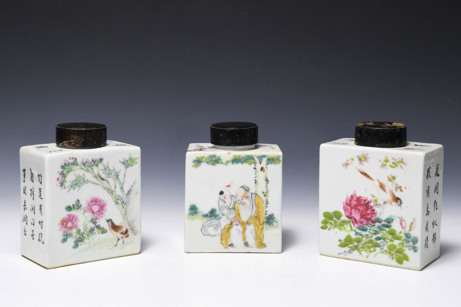 (3) Chinese Tea Caddies, Late 19th Century: (3) Chinese porcelain rectangular tea caddies, late 19th century, with figurative and floral vignette on front and back faces and characters over other faces. Lacquered wooden lids and wooden stands.