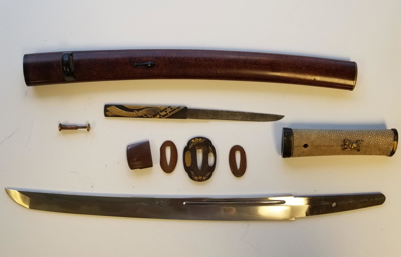 Japanese Wakizashi Sword & Kozuka Dagger: Japanese Wakizashi short sword & Kozuka dagger: Curved single edge blade with signed tang, iron tsuba with the image of flowers. The handle wrapped in shark-skin, with gilded menuki in the form of qil