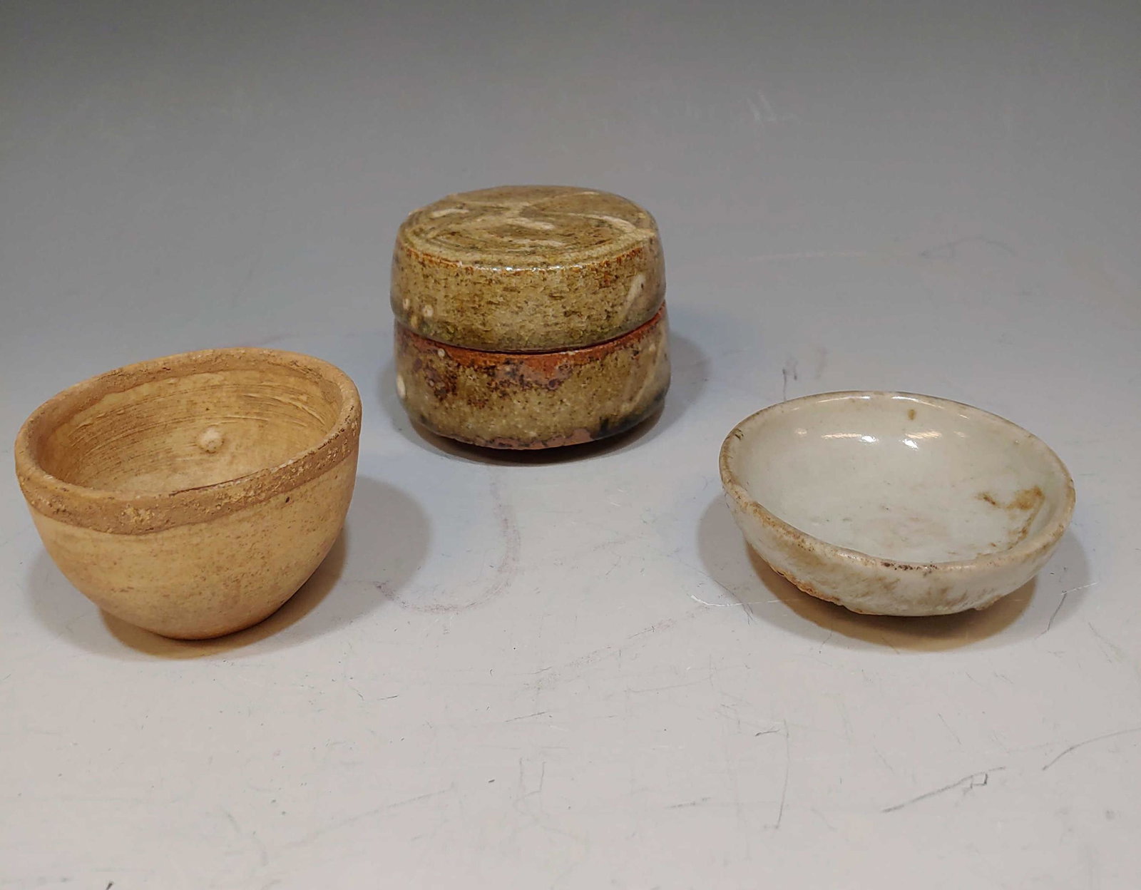 (3) 16th Century & Earlier Korean Ceramic Pieces: Group of (3) 16th century and earlier Korean ceramic pieces. Includes a small lidded jar with slip decoration in white, a small unglazed bowl, and a small shallow dish. Dimensions are: lidded jar - 2 