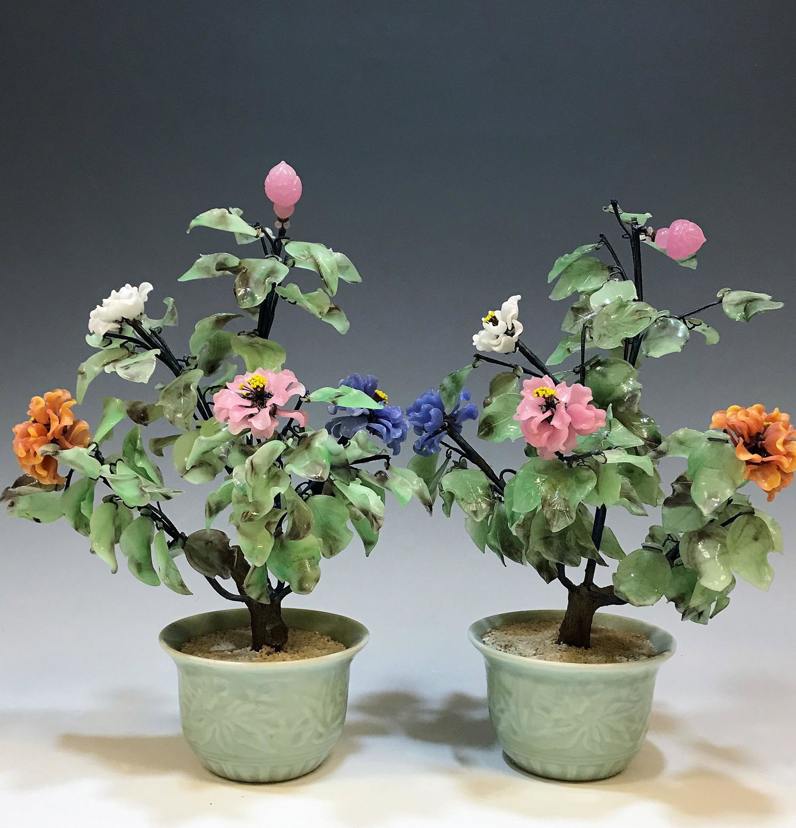 (2) Glass Flowers in Celadon Style Pots: (2) glass flowers in celadon style pots, glass flowers and buds are in shades of purple, orange, white, and pink. Dimensions are: 14 1/2 in (36.8 cm) tall X 8 in (20.3 cm) wide X 7 3/4 in (19.7 c) dee
