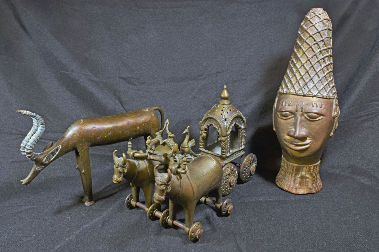 (3) African Benin Style Brass Figures: (3) African Benin style brass figures, includes: bronze head with detailing on the hair and surrounding the neck; horned animal figurine, potentially an antelope; two cattle attached to a closed carri