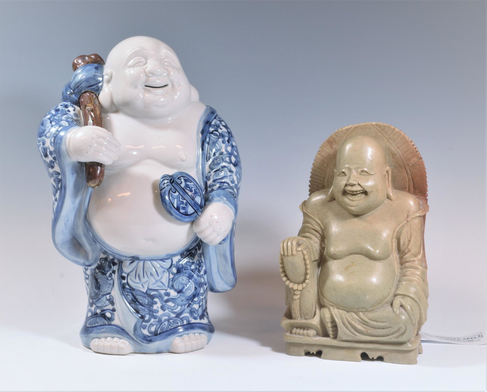(2) Chinese Budai, Porcelain & Soapstone: (2) Chinese Budai, porcelain and soapstone. A standing Budai figure made from blue and white porcelain. A seated Budai figure carved from soapstone. Dimensions are: 12 inches (30.5 cm) tall X 7 inches