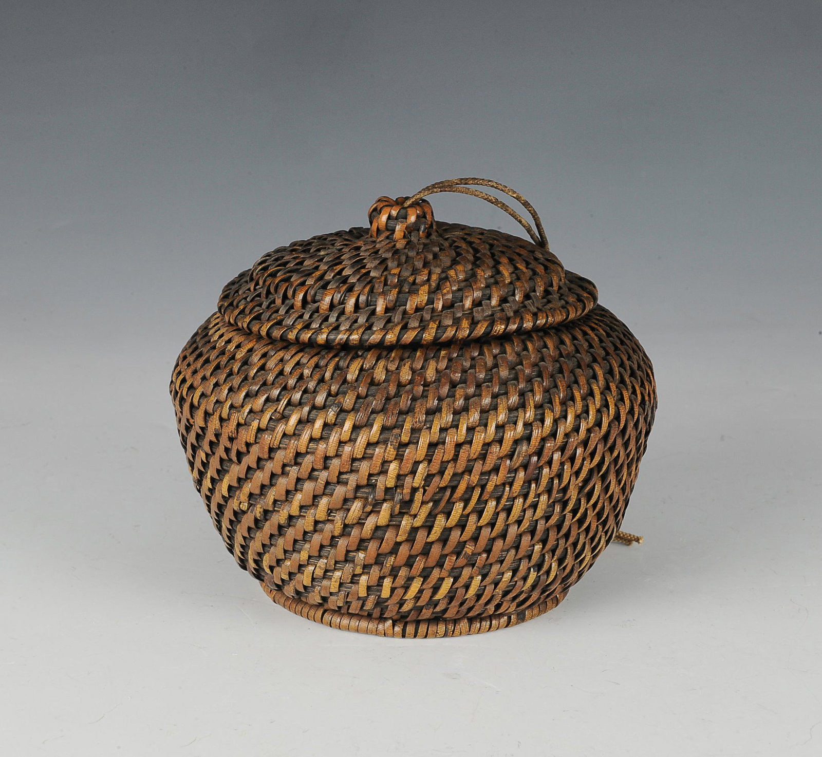 Chinese Rattan Basket w/ Good Luck Coins, 19th C: A Chinese rattan basket with a lid threaded with a string attached to 2 good luck coins on the bottom. Dimensions are: 4 inches (10.1 cm) tall X 5 inches (12.7 cm) diameter. All measurements are appro
