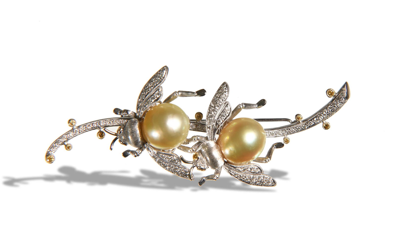 18K White Gold, Diamond, & Pearl "Bee" Brooch: Two bees on an 18K white gold stem with 105 pave diamonds, 1.1 ctw. The body of each bee is a 12-13 mm pearl. Stem and eyes are set with 13 yellow diamonds, .25 ctw. Dimensions: 3 inches long; 7.6 cm