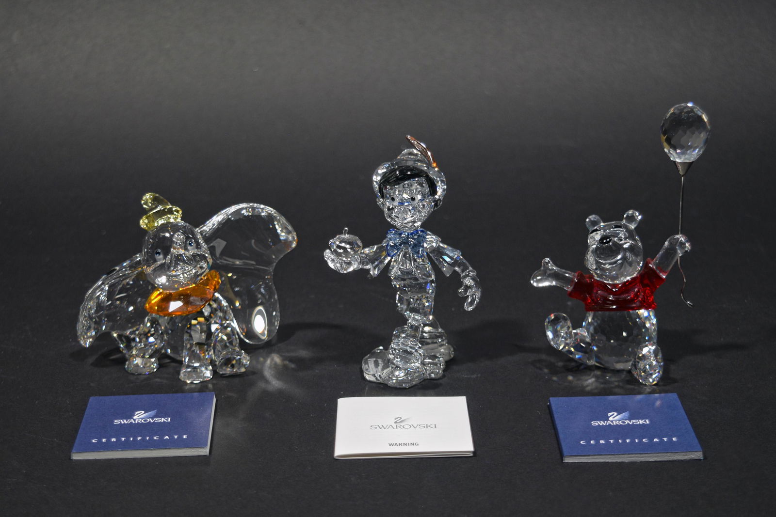 Swarovski, Pinocchio, Dumbo & Winnie the Pooh: Swarovski (Austrian, founded 1895) crystal. Includes a Dumbo figurine, Winnie the Pooh holding a balloon, and Pinnochio holding an apple. All figurines come with the original packaging and certificate