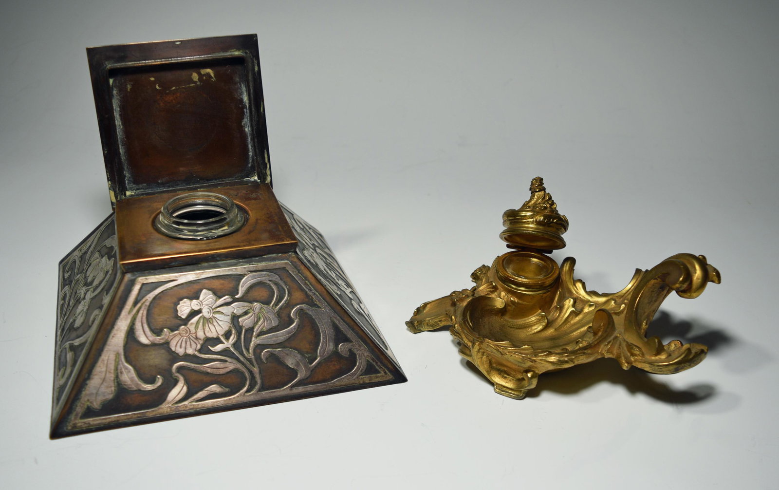 2 Bronze Art Nouveau Inkwells, Sterling Overlay: A set of 2 inkwells. Includes: a pyramid-form inkwell with sterling overlay, attributed to Heintz Metal Shops, and a bronze Rococo inkwell. Both are unmarked, but include the glass inserts. Dimensions