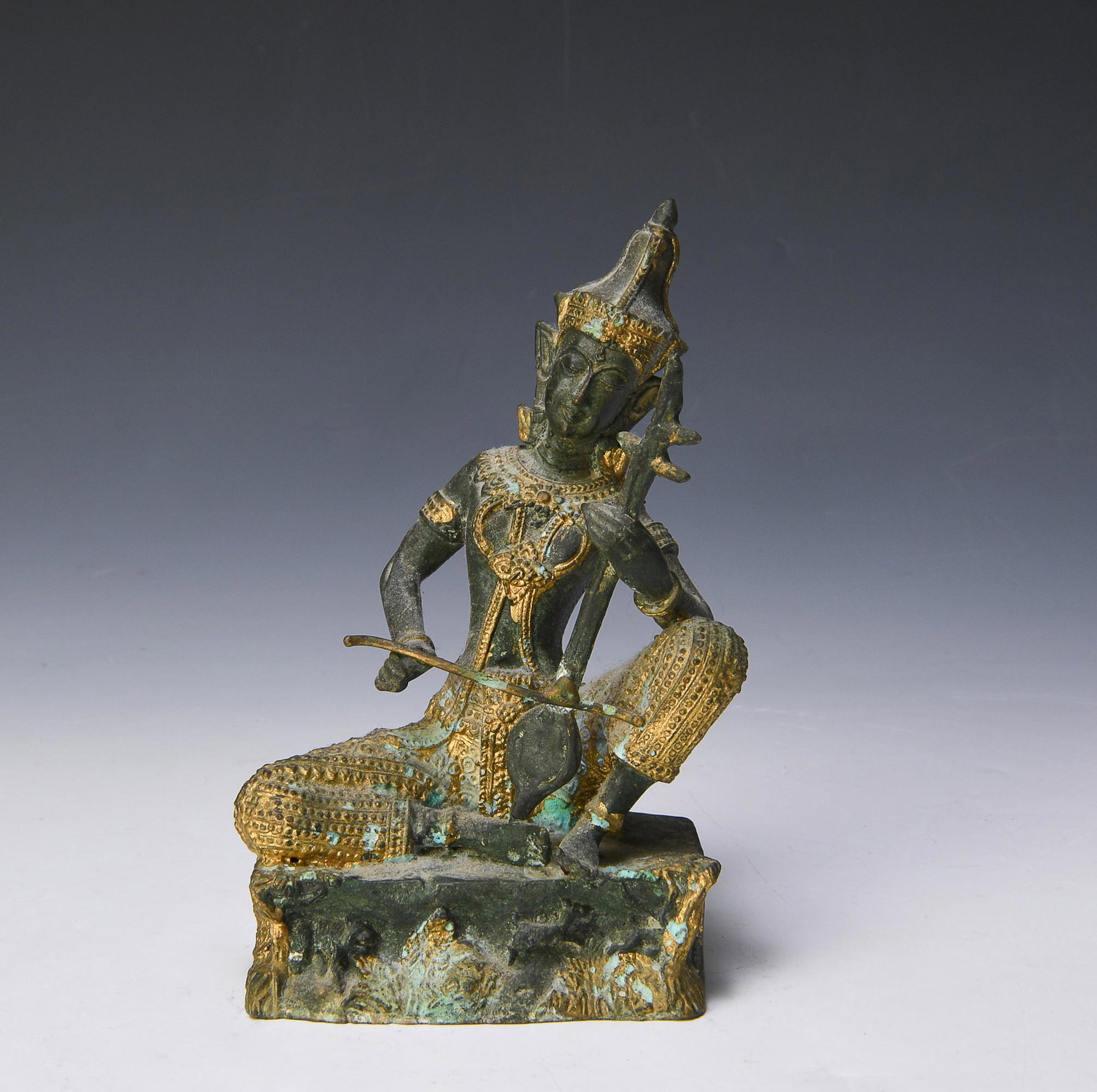 Thai Partial Gilt Bronze Musician, 19-20th Century: A Thai partial gilt bronze musician dating from the 19th to the 20th century. The musician is depicted in a seated position, playing the saw sam sai, and is dressed in chang kben with golden jewelry. 