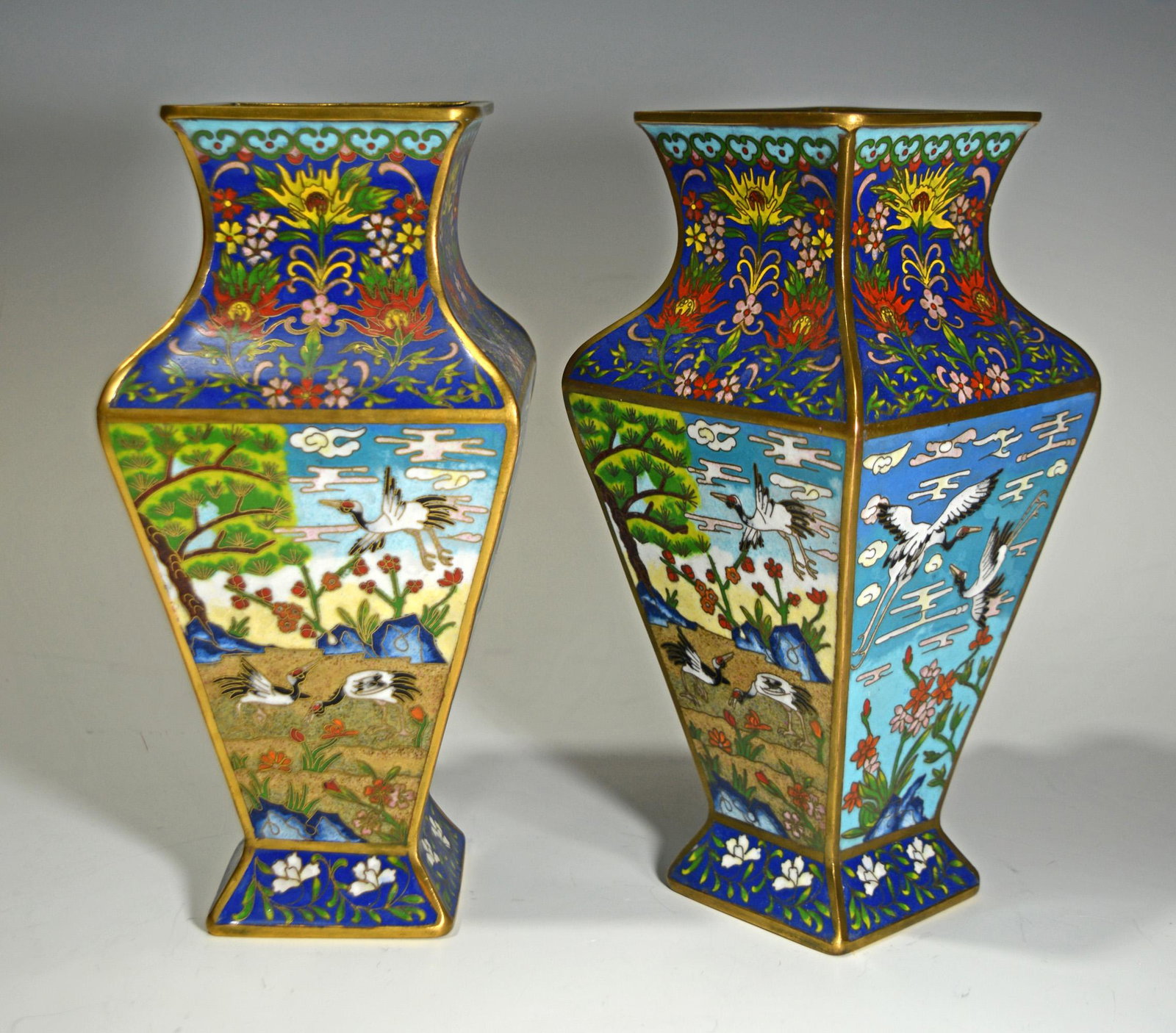 Pair of Elaborate Cloisonne Vases with Cranes: A pair of square cloisonne vases dating to the 20th century. The vases feature scenes of cranes and flowers on all four sides. Dimensions: 9 5/8 inches tall X 4 3/8 inches wide; 24.4 cm tall X 11.1 cm