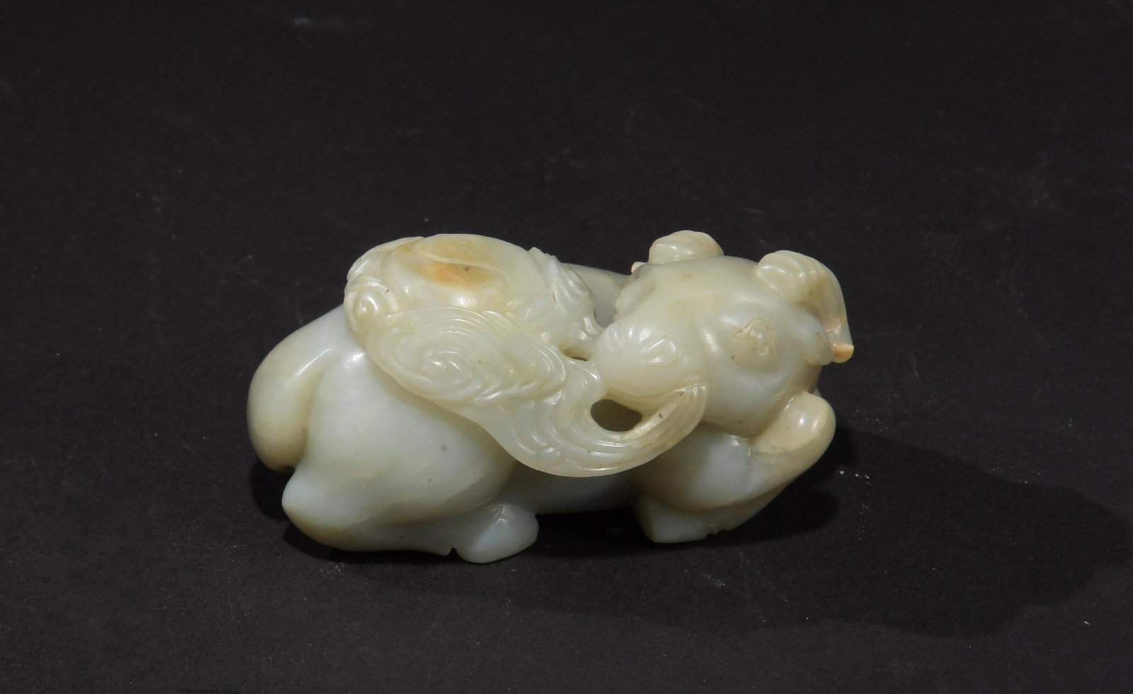 Chinese Carved Jade Goat, Early 18th Century: A Chinese jade carving dating from the early-18th century. The carving depicts a goat holding a lingzhi mushroom in its mouth and a yin-yang medallion on its back. Dimensions are: 1 1/2 inches tall X 