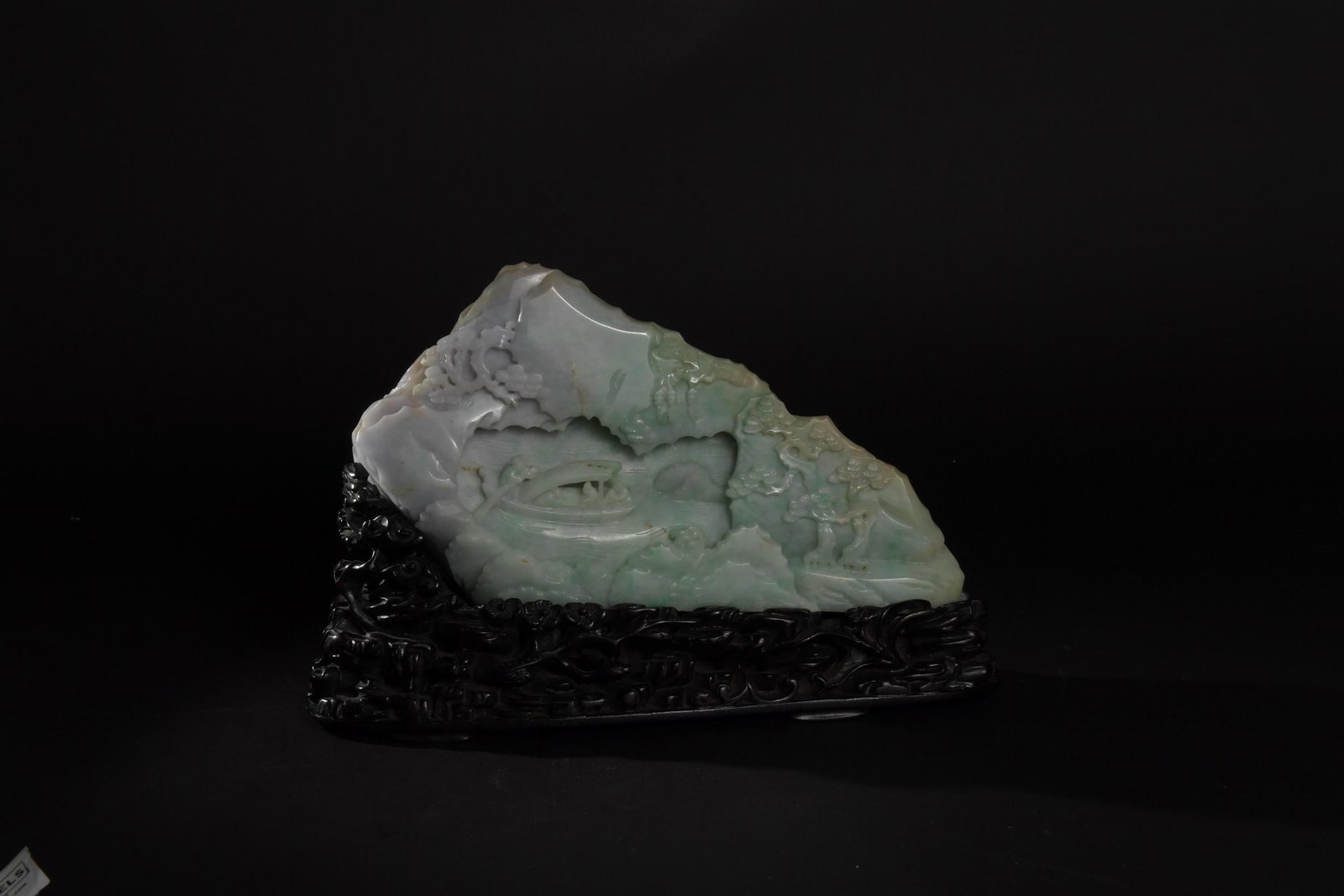 Chinese Jadeite Boulder, 19th Century: A Chinese carved jadeite boulder dating from the 19th century and with a fitted wooden stand. The front of the boulder features 6 figures in a mountain landscape beneath a pine tree. The other side fe