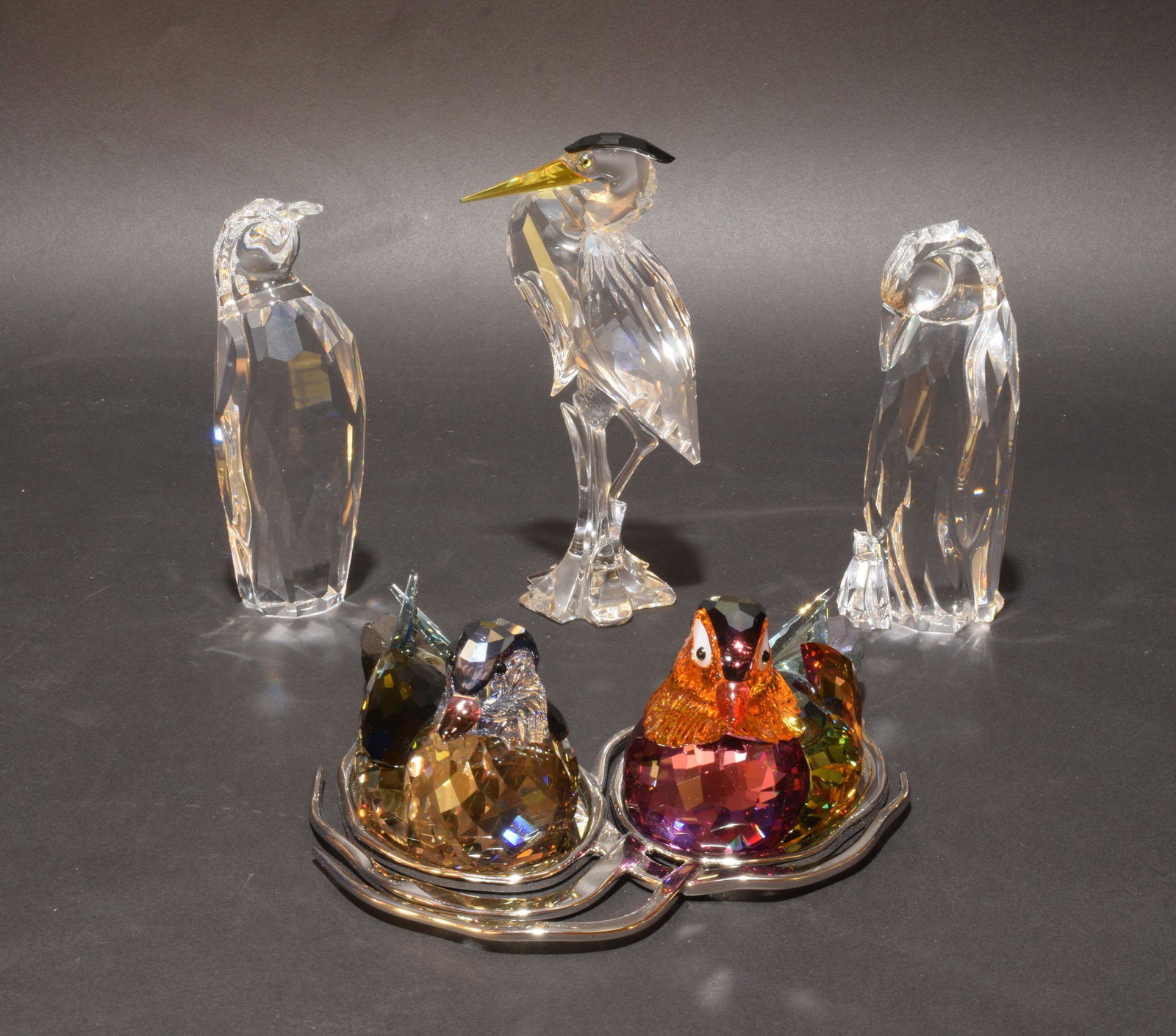 4 Boxed Swarovski Crystal Birds: Swarovski (Austrian, founded 1895) crystal. A group of bird figurines including: a mother penguin with a baby, a silver heron, a penguin, and a pair of colorful birds on a stand. All figurines come wi