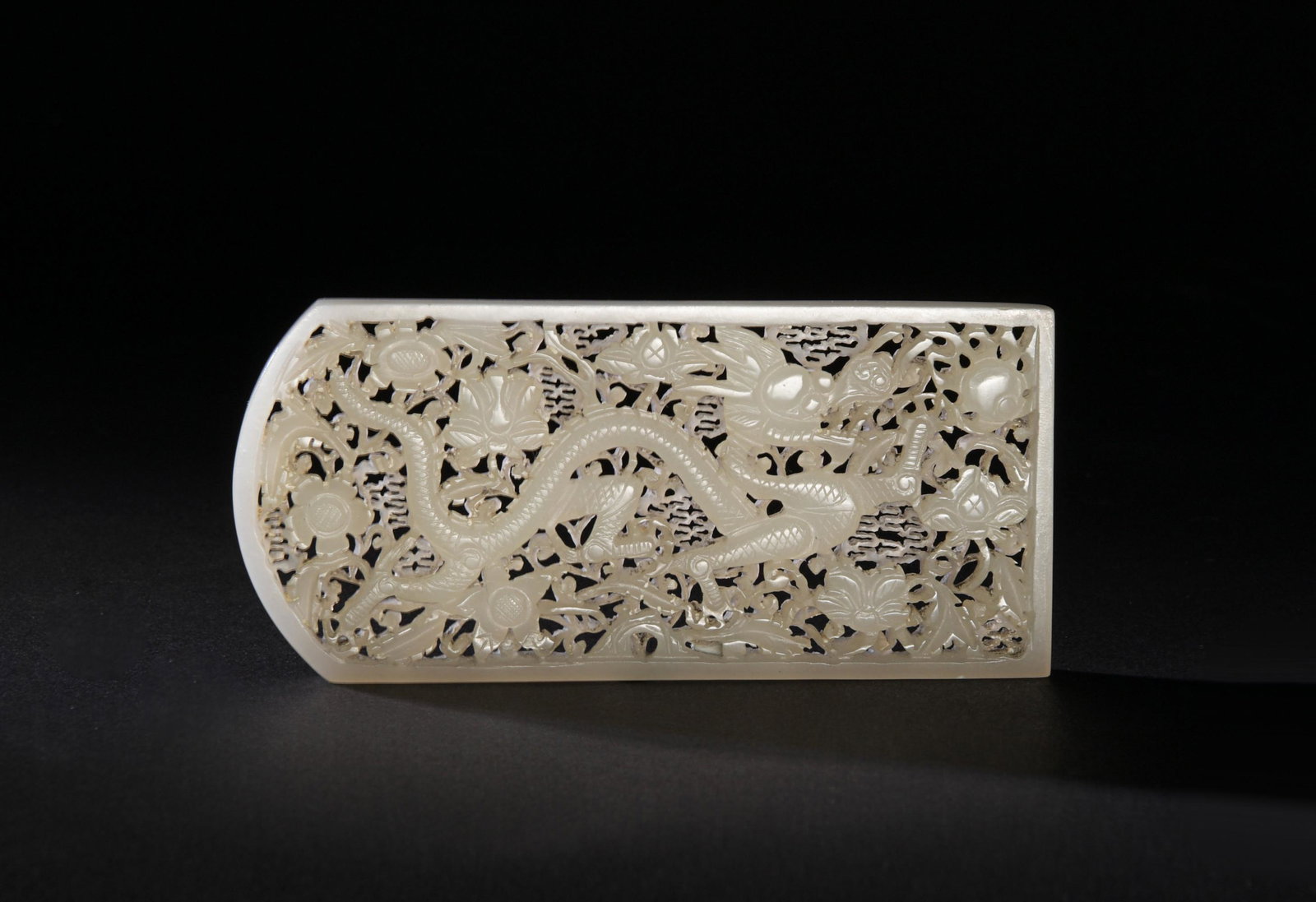 Chinese White Jade Plaque with Dragons, Ming: A Chinese white jade carved plaque dating from the Ming dynasty. The plaque features a 4-clawed dragon chasing a flaming pearl among floral tracery. Dimensions: 2 inches tall X 4 1/4 inches wide; 5.1 