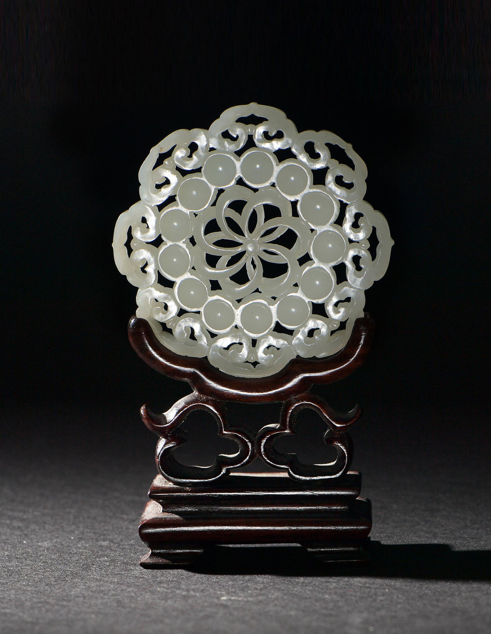 Chinese White Jade Pierced Plaque, Ming Dynasty: A Chinese white jade pierced flower-form plaque dating from the Ming dynasty. The plaque features a ruyi border and a central flower. It comes with a stand. Dimensions: 2 3/4 inches in diameter; 7 cm 