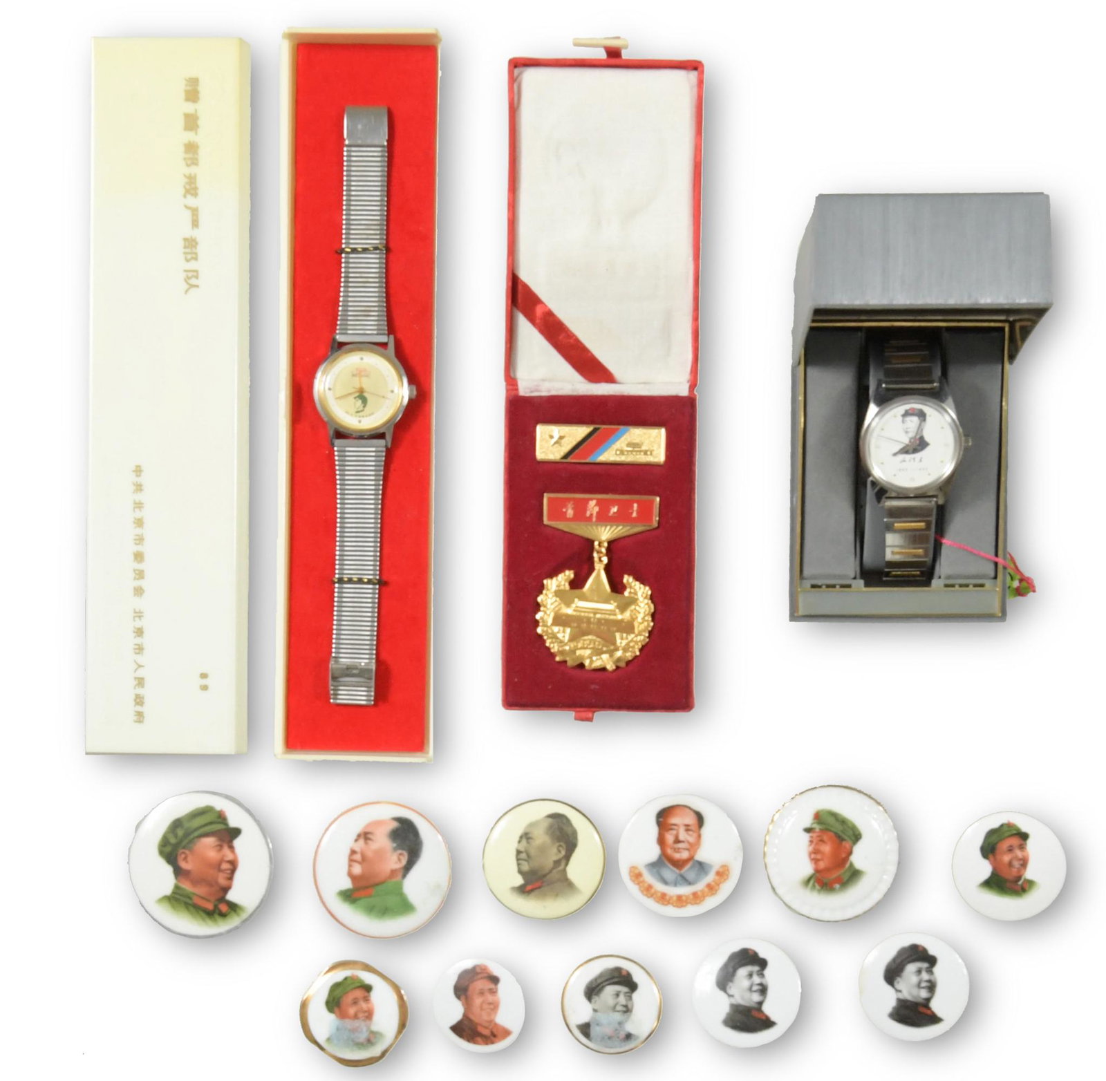 Collection of Mao Tse-Tung Emblems & Watches: A collection of emblems and watches. Includes: 11 porcelain Mao Tse-Tung emblems; a cased medal reading 'The Guardian of the Capital'; a cased wristwatch from Weishi Co. with tag; and a cased watch fr