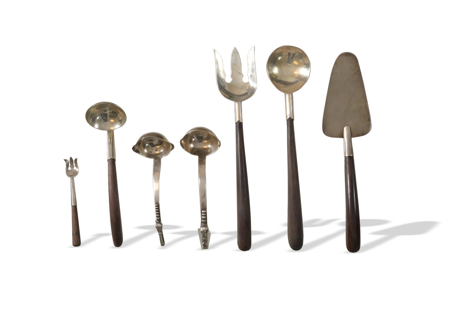 7 Taxco, Sanborns, Etc. Sterling Serving Pieces: Jose Anton, Taxco pie server, three Mexican sterling MCM serving pieces, and a small condiment fork, all with wood handles. Two Sanborns mid-century ladles with flower motif. Dimensions are: Largest, 