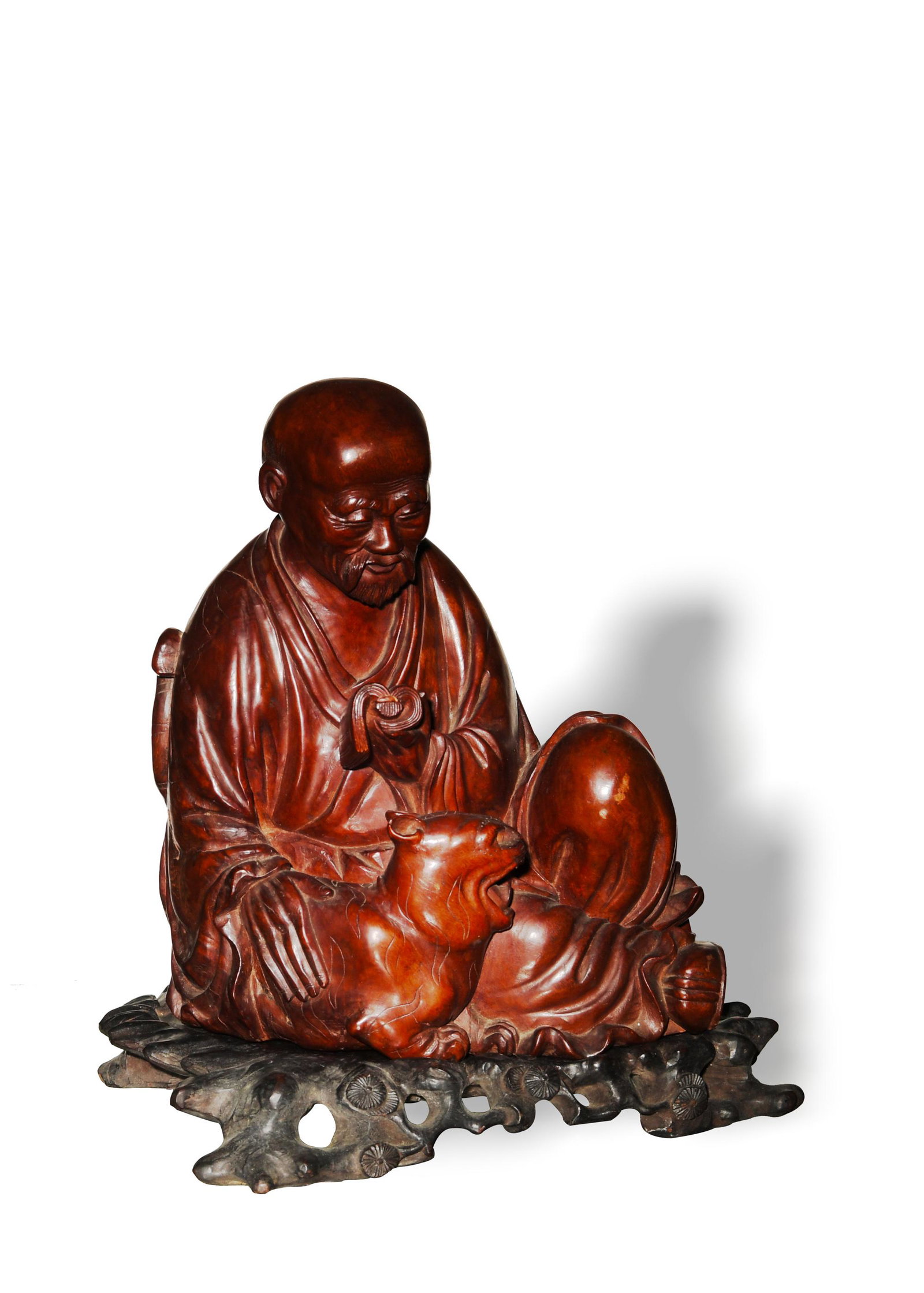 Chinese Hardwood Carved Luohan, 19th Century: A Chinese hardwood carving of the Tiger Taming Luohan dating from the 19th century with a wooden stand. The Luohan is holding a book in his left hand and leans against a tiger with his right hand. Dim