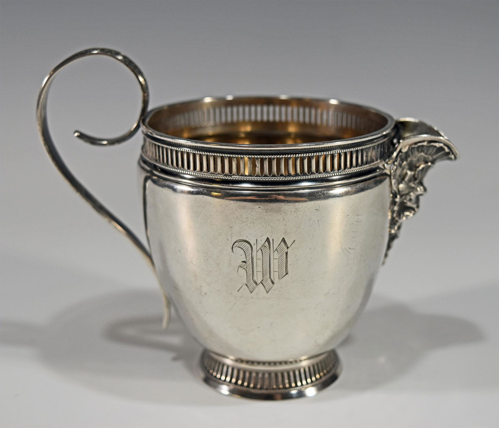 19th Century Gorham Creamer with Figural Spout: A 19th century Gorham creamer with a figural spout. The top and bottom rims have a pierced design and the body has a monogram. The bottom has a hallmark. Dimensions are: 5 1/2 inches wide X 4 3/8 inch